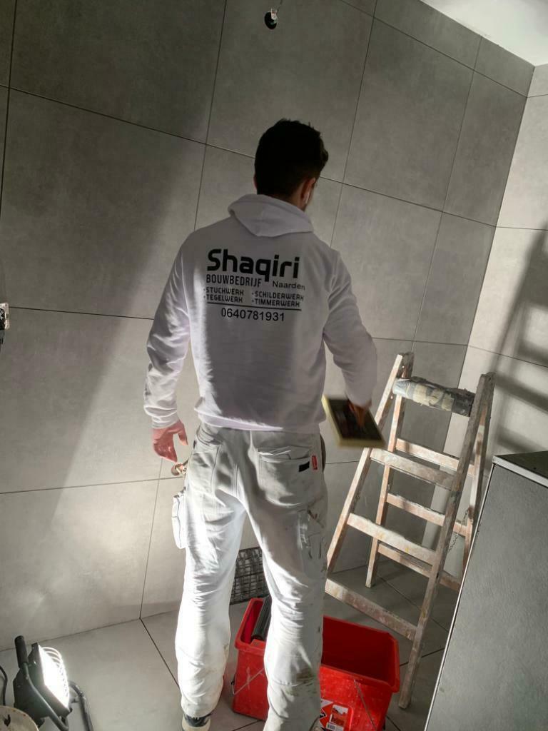 Shaqiri aan het tegelen in een hoodie van Shaqiri Bouwbedrijf